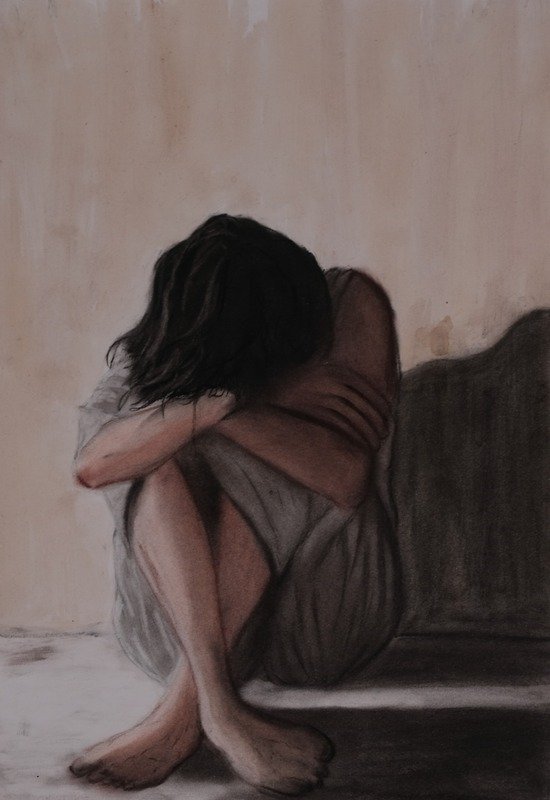 Figure assise au sol, les genoux repliés, le visage caché dans ses bras et ses cheveux.